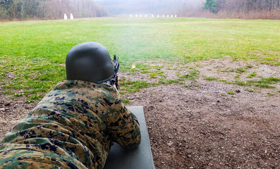 The soldier in the military department, with a helmet on his head, lies on the ground and targets...