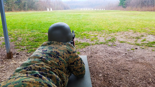 The soldier in the military department, with a helmet on his head, lies on the ground and targets the target