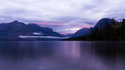 Fototapeta na wymiar Sunrise over lake at Glacier National Park. Purlpe tinted cloudy morning