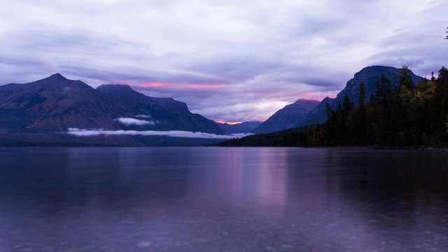 Sunrise over lake at Glacier National Park. Purlpe tinted cloudy morning © Brett