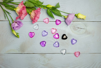 Pink and purple lisianthus (eustoma) flowers and glass hearts on a blue wooden table, top view, composition for St. Valentine's Day, Women's Day, etc.