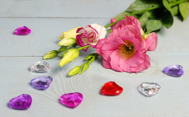 Flowering lisianthus (eustoma) and glass hearts on a blue wooden table, composition for St. Valentine's Day, Women's Day, etc.