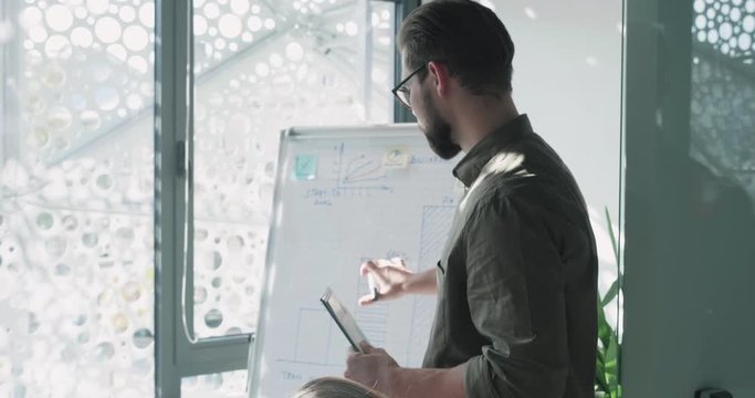 Portrait of Attractive Speaker Standing by Board with Marker and Tablet in his Hands, Looking Confident. Having Speak about new Projects and Proposing his Ideas. Teamwork. Business Lifestyle.