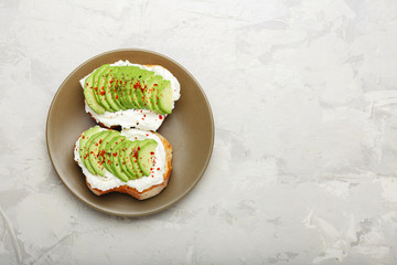 Two avocado toasts, avocado sandwich. Fresh avocado sliced on toast of wheat bread, cream cheese. Avocado sprinkled with chili, basil spices on a gray concrete background with place for text, top view