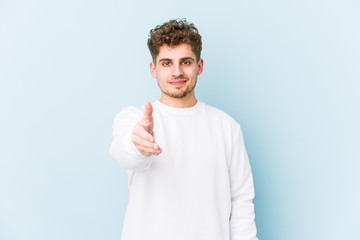 Young blond curly hair caucasian man isolated stretching hand at camera in greeting gesture.