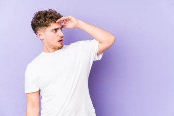 Young blond curly hair caucasian man isolated looking far away keeping hand on forehead.
