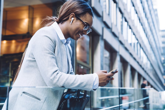Joyful adult ethnic woman interacting with smartphone while standing on street