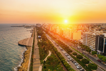 Obraz premium Aerial view of Limassol city coast in Cyprus. Walk path Molos Park with palm trees, Mediterranean sea and urban skyline at sunset, drone photo.
