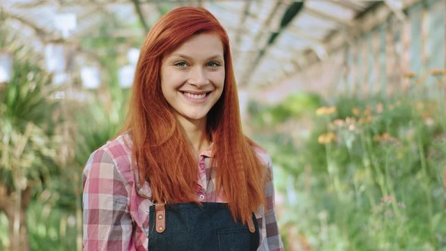 Portrait of a woman gardener smiling large in front of the camera she crossing hands and looking straight in the middle of flower greenhouse