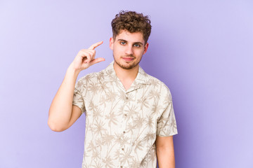 Young blond curly hair caucasian man isolated holding something little with forefingers, smiling and confident.