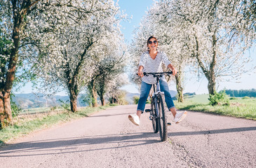 Fototapeta Happy smiling woman rides a bicycle on the country road under the apple blossom trees obraz