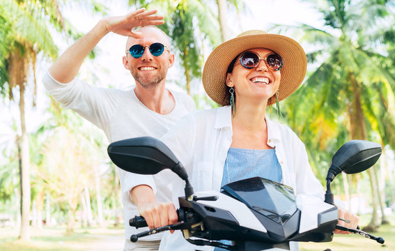 Happy smiling couple travelers riding motorbike scooter under palm trees. Thailand tropical vacation concept image