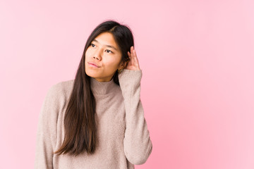 Young chinese woman posing isolated trying to listening a gossip.