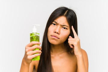 Young chinese woman holding a moisturizer with aloe vera isolated pointing his temple with finger, thinking, focused on a task.