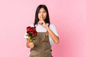 Young chinese gardener woman holding a roses isolated keeping a secret or asking for silence.
