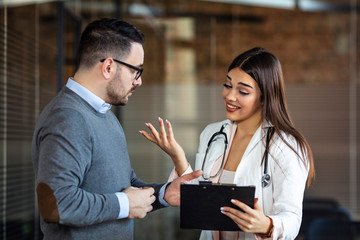 Charming female doctor giving advice to a male patient. Healthcare and medical concept - doctor with patient in hospital. Doctor and patient discussing.