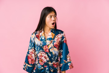 Young asian woman wearing a kimono pajamas being shocked because of something she has seen.