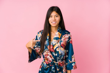 Young asian woman wearing a kimono pajamas person pointing by hand to a shirt copy space, proud and confident