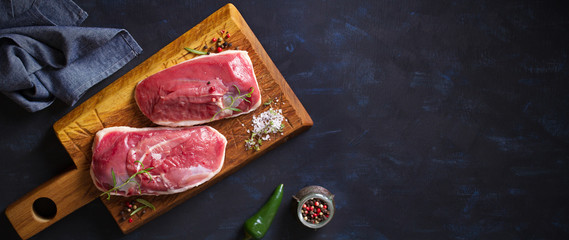 Raw fresh meat, duck breast fillet on wood chopping board with rosemary and seasons. Flat lay