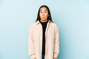 Fototapeta premium Young woman isolated on a blue background shrugs shoulders and open eyes confused.
