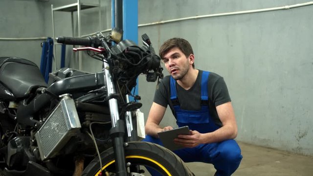 Mechanic with tablet tries to repair a motorcycle in car service