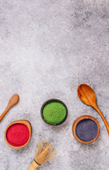 Obraz na płótnie Canvas Different colors of japanese matcha tea: green, red and blue in wooden bowls on gray background. Acai berry powder, green tea leaf powder, and clitoria flower powder. Top view. Flat lay. Copy space