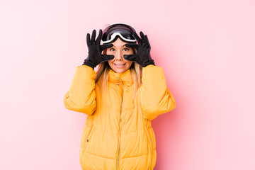 Young caucasian woman wearing a ski clothes in a pink background keeping eyes opened to find a success opportunity.