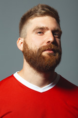 Obraz premium Portrait of proud handsome middle aged red-haired sportsman over gray wall. Red sportswear. Football player. Lumberjack style. Vertical studio shot