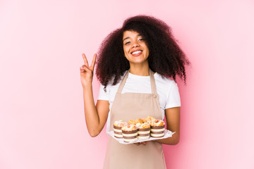 Young afro pastry maker woman holding a cupcakes isolatedYoung afro baker woman showing number two with fingers.