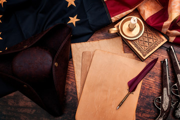 Federalist papers and the birth of the United States of America concept with tricorn hat, candle, feather quill, musket gun, the Betsy Ross American flag and aged paper with copy space - Powered by Adobe