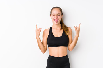Fototapeta na wymiar Young caucasian fitness woman posing in a white background showing rock gesture with fingers