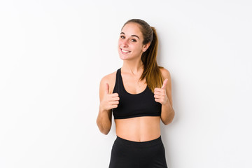 Fototapeta na wymiar Young caucasian fitness woman posing in a white background raising both thumbs up, smiling and confident.