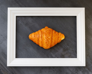 Classic french croissant in a white frame on a dark background. Design of a bakery, cafe, restaurant, kitchen. Horizontal shot. Close up. Handmade food with soul. Bakery at home. Bread business.