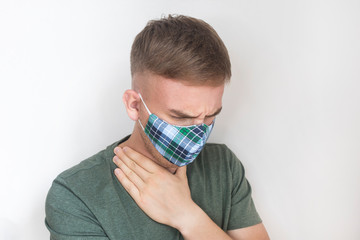 Young sick ill man, guy in protective mask on his face coughs, holding hands by the neck, suffering from cough, sore throat on white background. Cold, Chinese coronavirus virus, flu, disease concept.