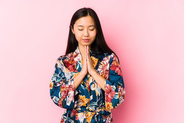 Young chinese woman wearing a kimono pajama isolated holding hands in pray near mouth, feels confident.