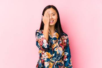 Young chinese woman wearing a kimono pajama isolated having fun covering half of face with palm.