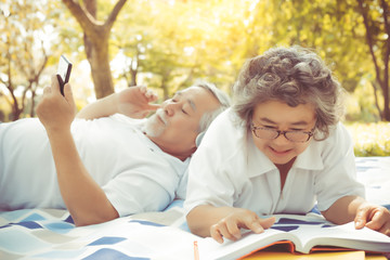 Old asian people, senior couple, elderly man and elderly woman get enjoying in park. Old husband listening music, lay down on old wife back. Grandma reading book, smile face. Senior couple happiness 