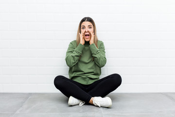 Young caucasian woman sitting on the floor shouting excited to front.