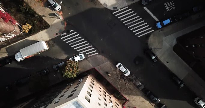 Cars drive on the roads of downtown Brooklyn New York City as bicycles and pedestrians use crosswalk casting shadows on the sidewalk. Aerial Drone