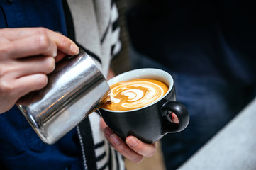 Barista making latte art by pouring fresh milk to coffee cup. Hot latte or cappuccino in ceramic black coffee cup.