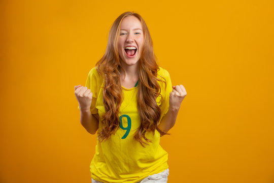 Brazil Supporter. Brazilian Redhead Woman Fan Celebrating On Soccer, Football Match On Yellow Background. Brazil Colors.