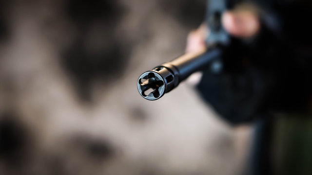 Armed security contractor holds barrel of an AR15 rifle to the camera with a shallow depth of field