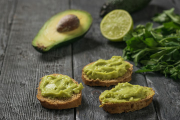 Three slices of bread with guacamole on a black wooden table. Diet vegetarian Mexican food avocado.