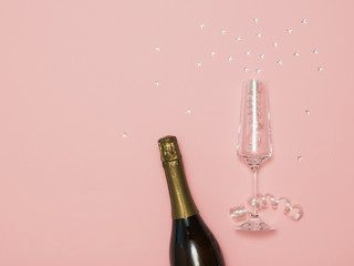 Fototapeta premium A bottle of sparkling wine and a glass with streamers and stars on a pink background.