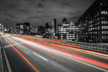 Manhattan bound traffic over the Brooklyn Bridge at night with a long exposure on the brake lights. City skyline in the background with the road in the foreground. 