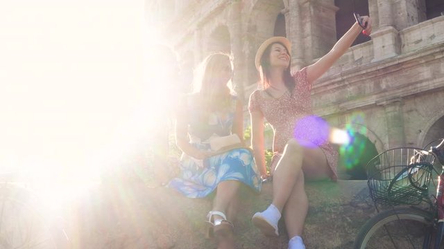 Three happy young women friends tourists with bikes taking selfies at Colosseum in Rome, Italy at sunrise.
