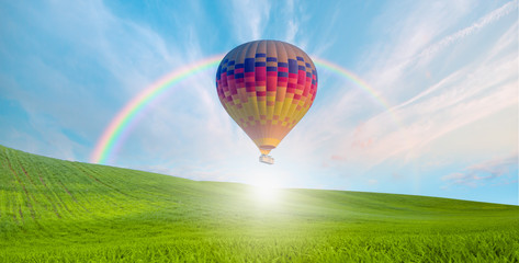 Hot air balloon flying over spectacular green grass field with rainbow