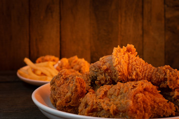 Fried chicken and French fries in white dish on wooden table with orange light.
