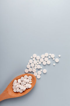 White pills in a wooden spoon on a pastel blue background. Flat lay, top view, layout, template, copy space. Pharmacy and medical concept