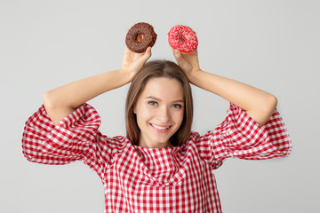 Funny young woman with tasty donuts on grey background